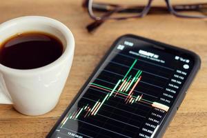 beurs grafiek op smart phone scherm kopje koffie en bril foto