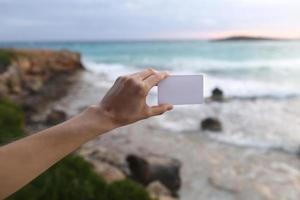 vrouwelijke hand met een wit visitekaartje of een notitie met plaats voor tekst op de strandachtergrond en de zee die golven maakt. selectieve aandacht