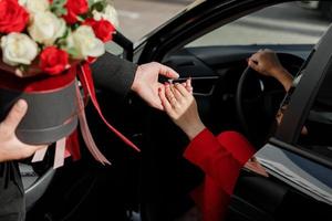 beleefde man met een boeket bloemen helpt een zakenvrouw in een rood pak om uit een parkeerplaats buiten te komen