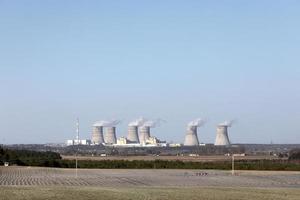 weergave van een kerncentrale. weergave van rokende schoorstenen van een kerncentrale, elektrische leidingen en bos, onder blauwe hemel met witte wolken. foto