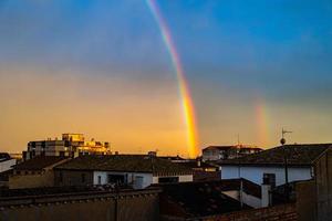 landschap met zonsondergang Aan een regenboog over- de daken van huizen in een Spaans stad- foto