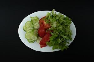 een foto van komkommers, tomaten en sla Aan een bord Aan geïsoleerd zwart achtergrond papier, na sommige bewerkingen.