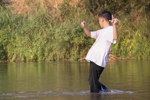 Aziatisch jongen is uitgeven zijn vrije tijd door duiken, zwemmen, het werpen rotsen en vangen vis in de rivier- gelukkig, hobby en geluk van kinderen concept, in beweging. foto