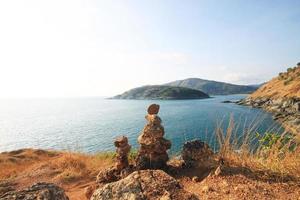 mooi piramide vorm van stenen geregeld met Boeddha standbeeld in zen Aan rots berg in zeegezicht van zonsondergang en zee horizon met droog gras veld- Aan phrom de P kaap in phuket eiland, Thailand. foto