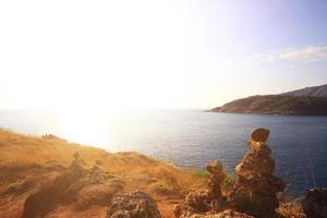 mooi piramide vorm van stenen geregeld met Boeddha standbeeld in zen Aan rots berg in zeegezicht van zonsondergang en zee horizon met droog gras veld- Aan phrom de P kaap in phuket eiland, Thailand. foto