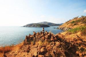 mooi piramide vorm van stenen geregeld met Boeddha standbeeld in zen Aan rots berg in zeegezicht van zonsondergang en zee horizon met droog gras veld- Aan phrom de P kaap in phuket eiland, Thailand. foto