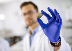 jonge wetenschapper houdt een mineraal specimen in beschermende handschoen bij material science lab
