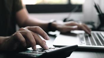 close-up van handen op een rekenmachine en laptop foto