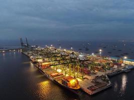 Jakarta, Indonesië 2021 - luchtfoto van het laden en lossen van containerschepen in de diepzeehaven, logistieke import en export van vrachtvervoer per containerschip op open zee 's nachts foto