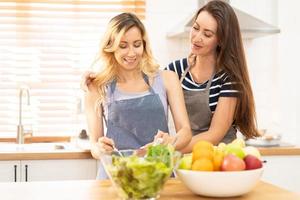 gelukkig en glimlach lesbienne paar Koken salade in de keuken. salade in glas kom met zoet glimlach terwijl Koken samen. trots maand naar promoten gelijkheid en verschillen van homoseksueel. foto