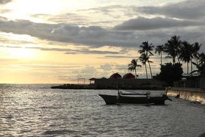 silhouet van een vissers boot en een kokosnoot boom Aan de strand met een zonsondergang achtergrond foto