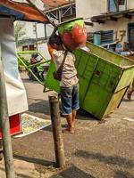 soera, Indonesië - april, 2023 - een dustman wie gooit vuilnis in de uitschot kar foto