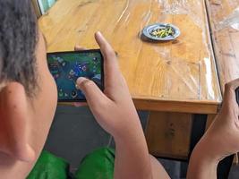soera, Indonesië - april, 2023 - een Aziatisch jongen spelen mobiel legends spellen Aan smartphone foto