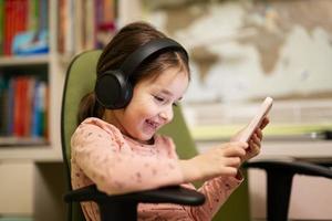 weinig meisje slijtage hoofdtelefoons aan het kijken tekenfilms of kind video Aan haar telefoon. foto