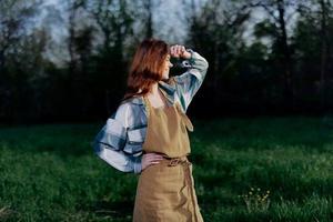 vrouw boerderij arbeider in schort ontspannende in natuur en aan het kijken de zonsondergang na een dag van werk Aan de boerderij foto