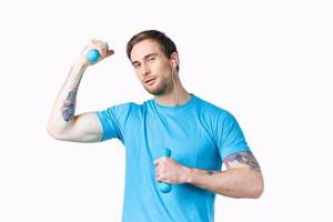 Mens met halters gemotiveerd omhoog arm spieren glimlach model- tatoeëren blauw t-shirt foto