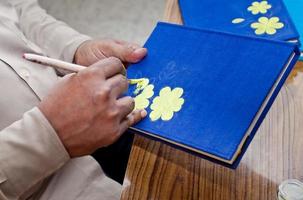 een handwerk artiest is schilderij Aan een handgemaakt boek Hoes in huis studio werkruimte. foto