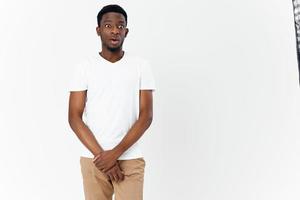 een bescheiden Afrikaanse Mens in een wit t-shirt en beige broek houden zijn handen in voorkant van hem Aan een licht achtergrond foto