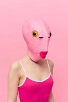 grappig gek vrouw Aan een roze achtergrond staand in een vis hoofd masker Aan een roze achtergrond, conceptuele halloween kostuum kunst foto