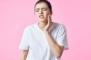 vrouw in wit t-shirt Holding haar nek pijn problemen roze achtergrond foto