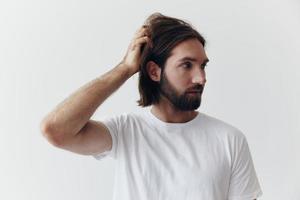 portret van een Mens met een zwart dik baard en lang haar- in een wit t-shirt Aan een wit geïsoleerd achtergrond emotie van droefheid en verlangen foto