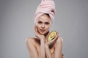 mooi vrouw naakt schouders met handdoek Aan hoofd avocado in hand- bijgesneden keer bekeken van grijs achtergrond foto