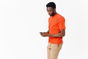 Afrikaanse Amerikaans in een t-shirt met een mobiel telefoon in zijn hand- Aan een licht achtergrond foto