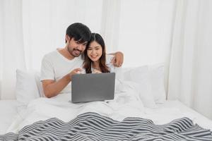 jong gelukkig Aziatisch paar gebruik makend van laptop in bed aan het kijken film, romantisch tijd naar verbeteren familie relatie, familie concept. foto