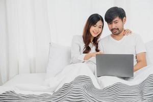 jong gelukkig Aziatisch paar gebruik makend van laptop in bed aan het kijken film, romantisch tijd naar verbeteren familie relatie, familie concept. foto