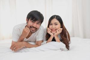 gelukkig jong Aziatisch paar omarmen, plagen, spelen vrolijk in bed Bij huis, romantisch tijd naar verbeteren familie binding. familie concept. foto