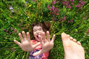 portret van een kind meisje in zomer aan het liegen in de gras en wilde bloemen met hakken en handpalmen. zomer tijd, vrijheid foto