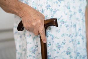 Aziatisch ouderen onbekwaamheid vrouw Holding wandelen stok, hout riet, ronde handvat, wandelen steun voor helpen naar wandelen. foto