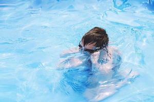 jongen duiken in zwemmen zwembad met zwemmen bril. jongen zwemt in de zwembad. kind aan het leren naar zwemmen foto