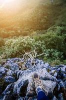 Gesloten omhoog wandelen schoenen van vrouw en staand Aan rots klif terwijl mooi zonsopkomst schijnend naar Woud Aan de berg. succes leven en vrijheid concept. foto