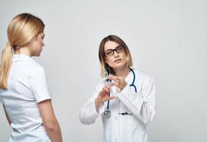 een vrouw verpleegster houdt een injectiespuit in haar hand- Aan een licht achtergrond met een stethoscoop en een vrouw geduldig foto