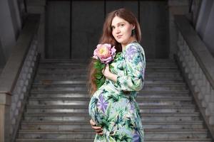 mooi zwanger vrouw met een bloem Aan een achtergrond van grijs trap. foto