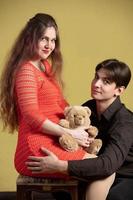 een knap Mens knuffels een mooi zwanger vrouw en een teddy beer. foto