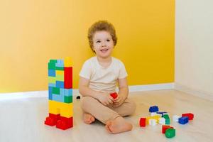 kind is spelen met kleurrijk kubussen Bij de tafel. kind heeft pret en bouwt van helder bouw blokken. vroeg aan het leren. leerzaam speelgoed foto