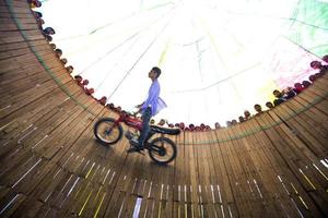 Bangladesh februari 14, 2018 een landelijk stunt fietser is riskeren zijn leven door schalen de muur van een groot houten goed in een motor carnaval bijzaak Bij bogoera, dhaka. foto