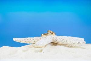 bruiloft gouden ringen Aan wit zeester Aan zanderig strand. marinier decor met accessoires voor tropisch bruiloft ceremonie Aan zomer achtergrond in heet land. reis, kom tot rust, huwelijksreis foto