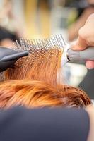 detailopname van meester hand- met föhnen en haarborstel blazen vrouw rood haar- in een salon. foto