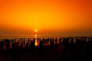 menigte van silhouet mensen wandelen Aan de het langst strand gedurende zonsondergang Bij chattogram. foto