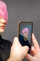 Mens kapper handen nemen afbeelding Aan smartphone van haar cliënt kort roze kapsel. foto