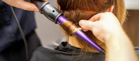 dichtbij omhoog van Haarstylisten handen gebruik makend van een curling ijzer voor haar- krullen in een schoonheid salon. foto