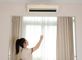 jonge Aziatische kamermeisje opent airconditioner met afstandsbediening in de hotelkamer foto