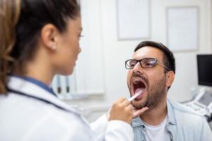 mannetje geduldig opening zijn mond voor de dokter naar kijken Bij zijn keel. vrouw dokter onderzoeken zeer keel van geduldig in kliniek. otolaryngoloog onderzoekt zeer keel van geduldig. foto