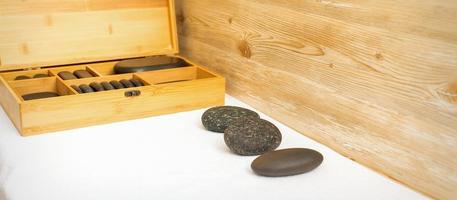 zwart massage stenen aan het liegen in de buurt de houten doos met massage rotsen Aan de handdoek Aan de tafel. foto