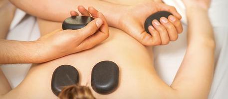 heet steen massage Aan de vrouw terug met handen van masseur Holding zwart massage stenen in spa salon. foto