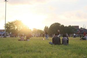 mensen zijn zittend Aan de gras Bij de zonsondergang veld- foto