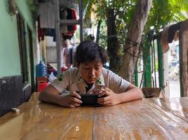 soera, Indonesië - april, 2023 - een Aziatisch jongen is op zoek Bij zijn smartphone foto